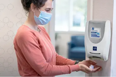 Healthcare facility visitor using wall-hung hand sanitizer dispenser