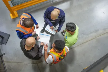 health-safety Birds-eye view of five workers in a warehouse discussing an issue while looking at instructions.