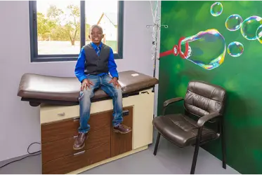 A young male child sits on a brown exam table in a doctor’s office.