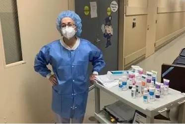 Caregiver wearing full PPE stands next to a rolling care full of Remedy products