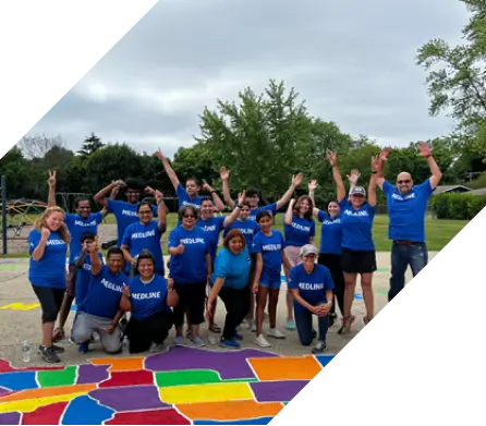 people-comm-bnr Medline employees in blue shirts posing in front of a colorful map painted on ground outside.