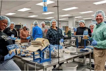 A group of volunteers wearing hair masks and gloves work together to package donations.