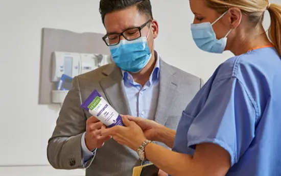 skin-care-specialist A man in a sport jacket and a clinician holding a Remedy product discuss it as she points to the label.