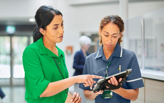 Two caregivers in hallway review CLABSI data on tablet