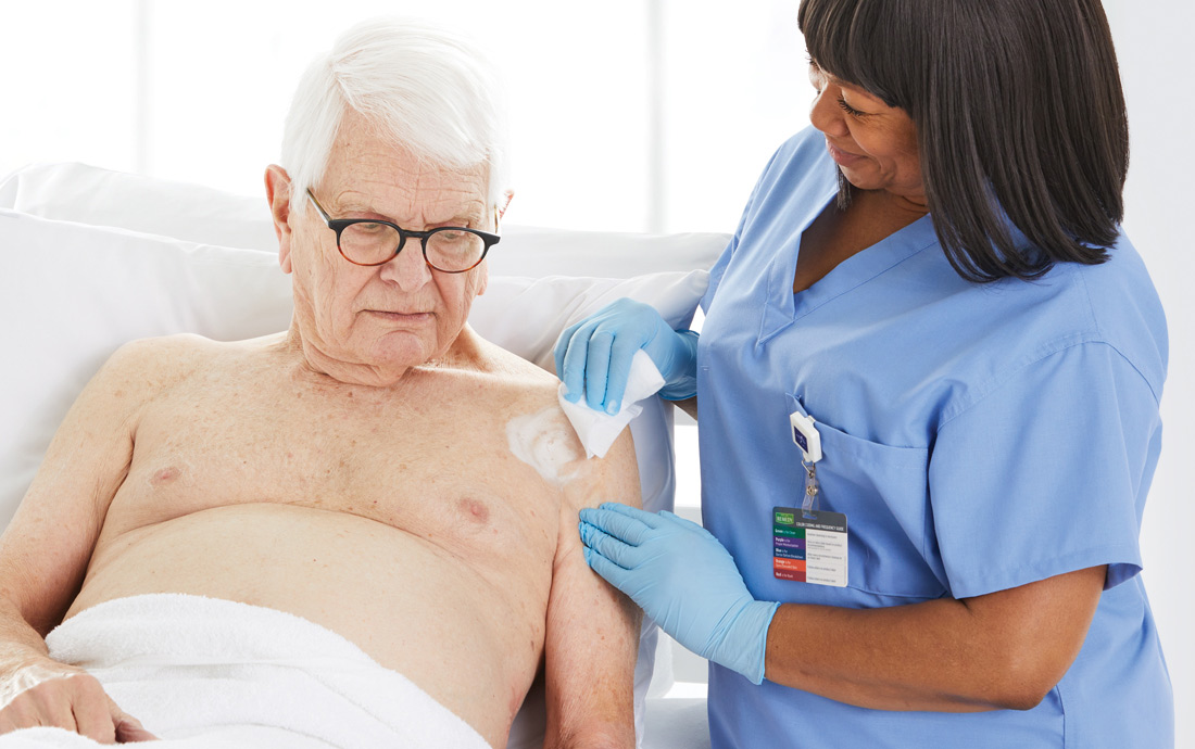 connect Smiling clinician cares for elderly, bedridden man by applying lotion on his affected shoulder.