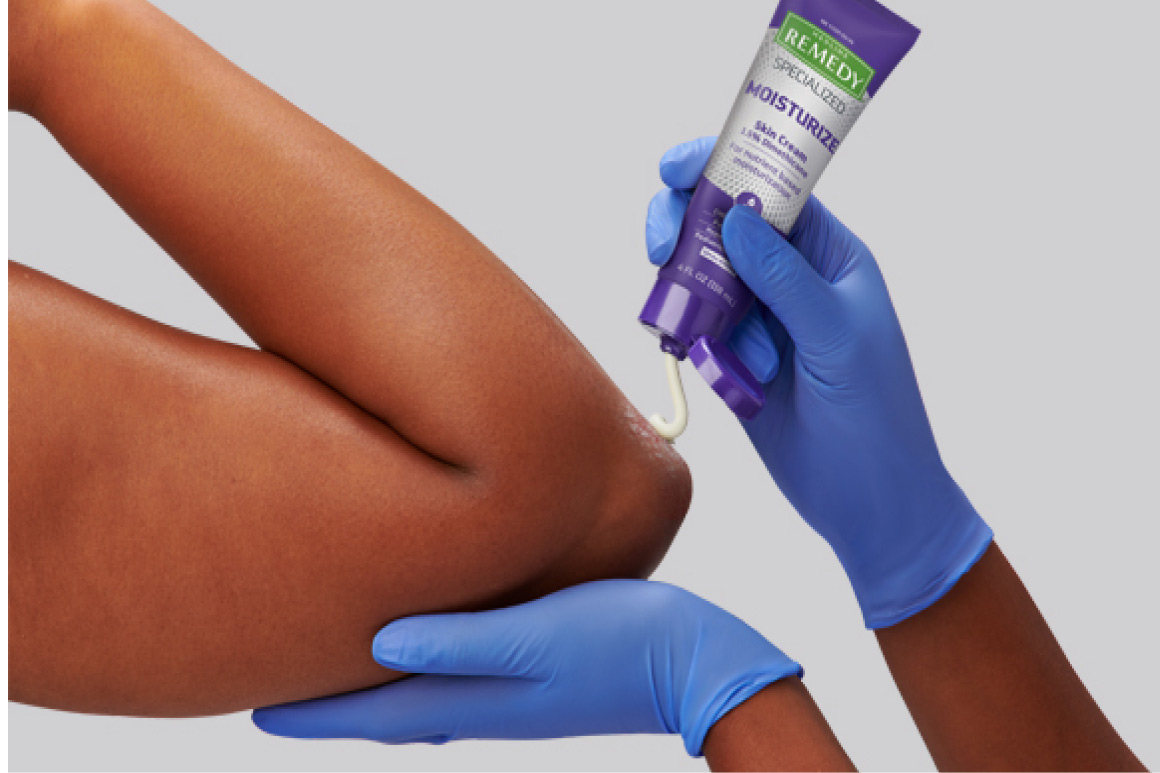 Gloved clinician hands apply Remedy moisturizer to dry skin on patient’s elbow.