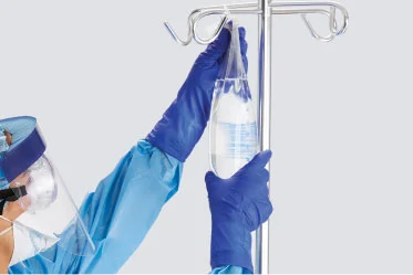 safety-with-quality Clinician wearing PPE, including gloves, hangs a bag of fluids from intravenous pole