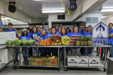 A photo of a large group of smiling workers standing behind a counter fulll of fruit