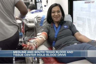 A photo of a smiling woman on a hospital bed giving blood at a blood drive