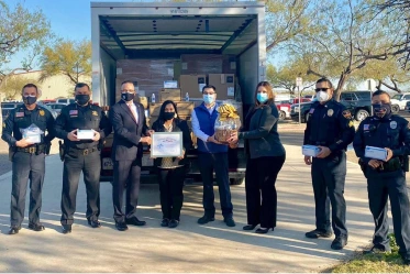 A photo of policman holding boxes of facemasks standing in front of a medical supply delivery truck